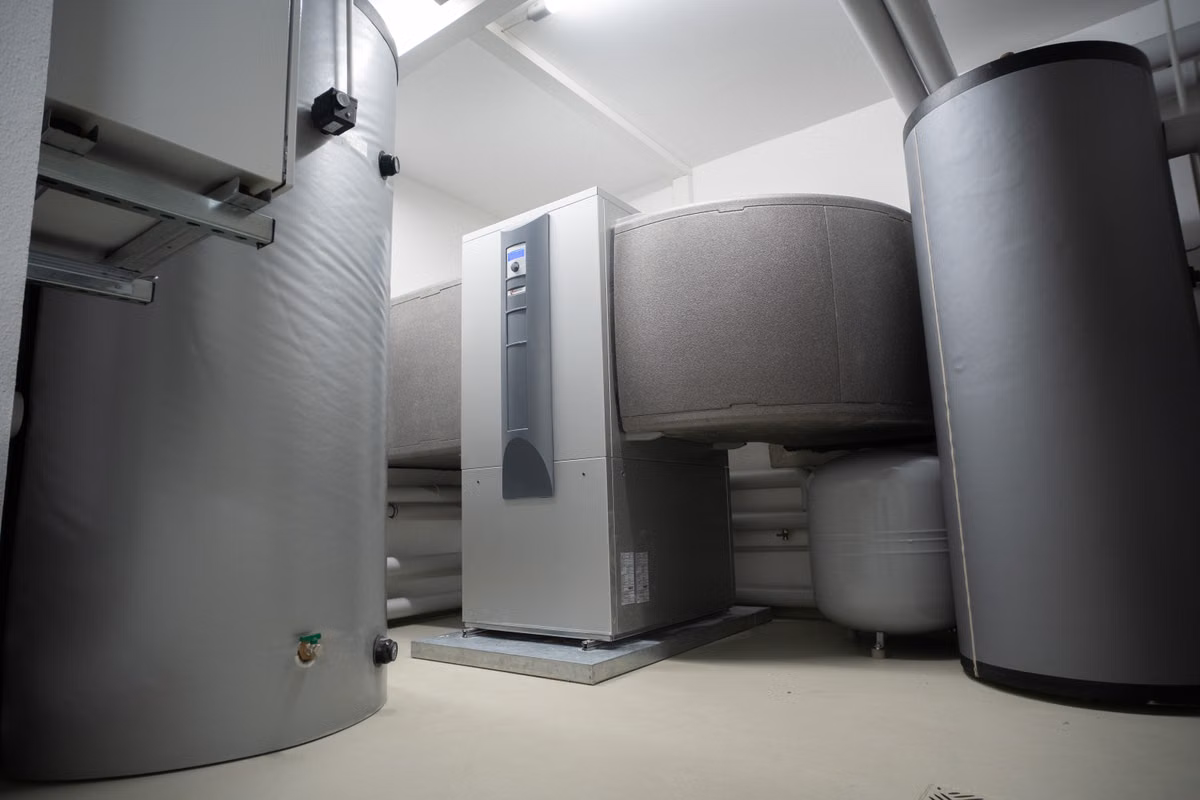 A plant room containing a floor-standing heat pump unit between insulated hot water storage cylinders and pipework.