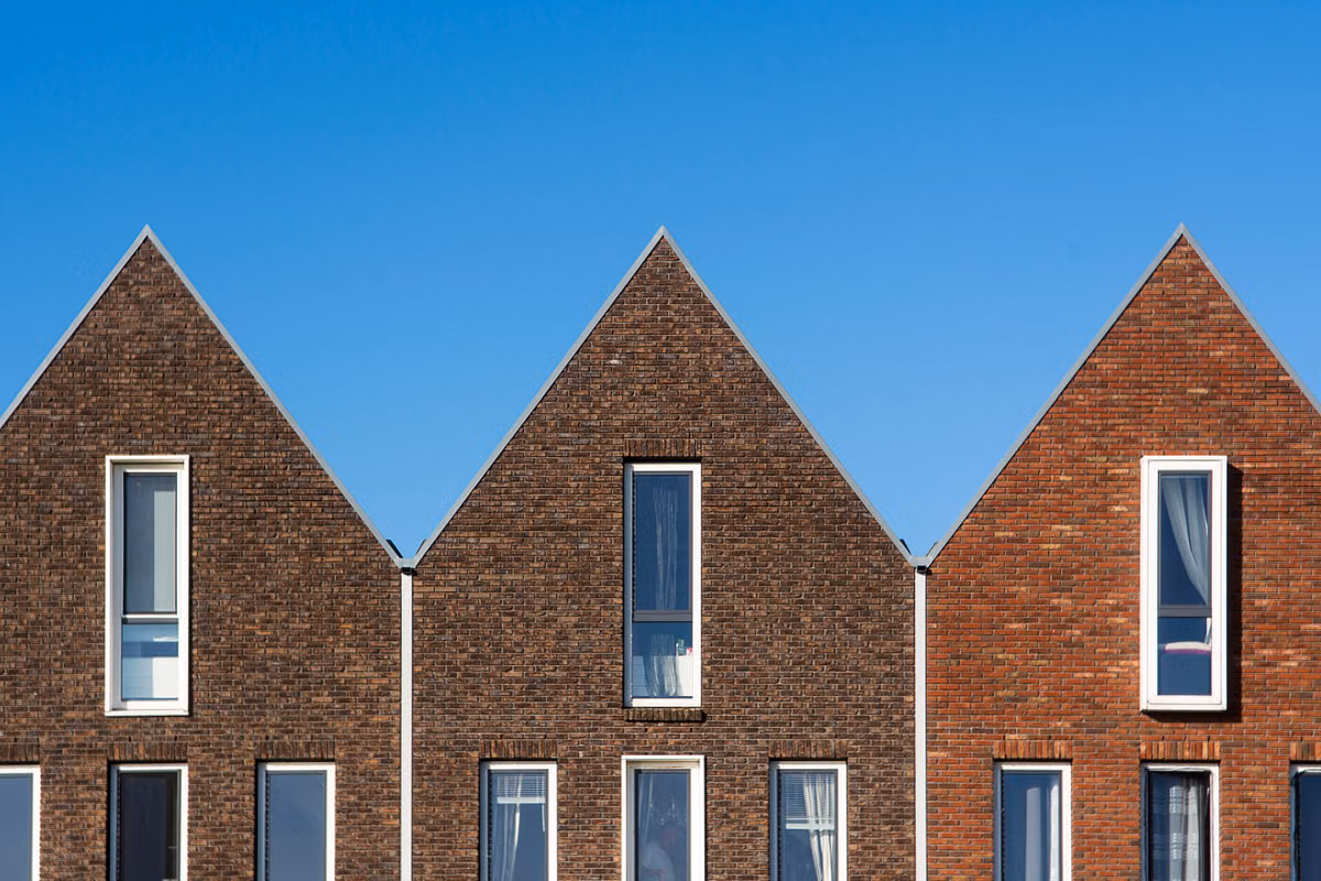A row of three modern brick terraced houses with steep gables and tall narrow windows against a clear blue sky.